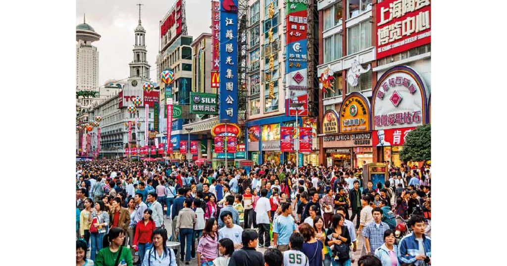 A bustling street filled with a large crowd of people walking in various directions, showcasing urban life and diversity.