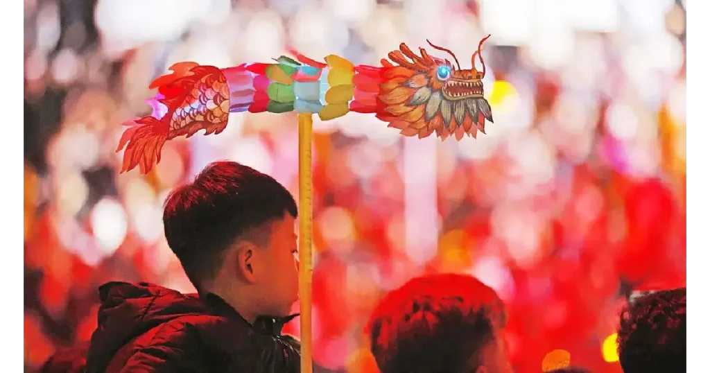 A boy proudly holds a small dragon amidst a lively crowd, symbolizing cultural significance in Chinese-speaking countries.